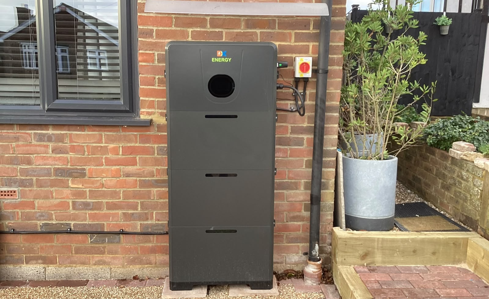 Front view of the slim charcoal battery installed against an exterior brick wall